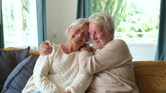Senior couple embracing tenderly while resting together on cozy living room couch, expressing affection and enjoying peaceful retirement moments inside their comfortable house