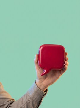 Red square speech bubble held aloft by hand against mint green background representing important announcements and brand communication.