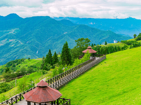 Wooden walkway and pavilions on a green hillside with mountain views