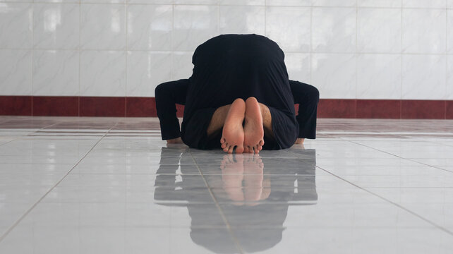 Person Performing Sujud Prayer on Tiled Floor in Mosque