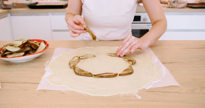 Pie preparation. Kitchen technique. Woman baker hand placing circle with fried pear pieces on flattered dough on bakery parchment.