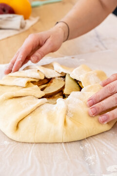 Fruit pastry. Cooking pie. Female baker hand preparing sweet round galette with pear pieces raw dough on on kitchen paper parchment.