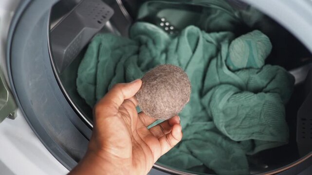 Hand holds a wool dryer ball beside laundry in a washing machine