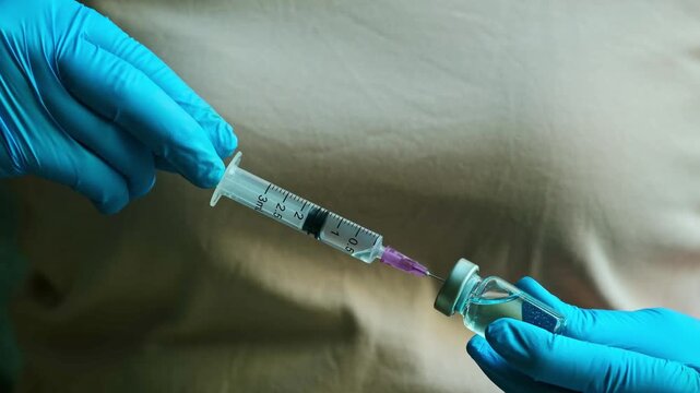 Medical woman professional wearing blue gloves preparing a vaccine injection by drawing medicine from a vial into a syringe, representing concept healthcare, vaccination, and medical procedures.
