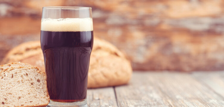 Dark ale in a clear glass with pale foam, paired with rustic bread on weathered wood, evoking a hearty pub meal
