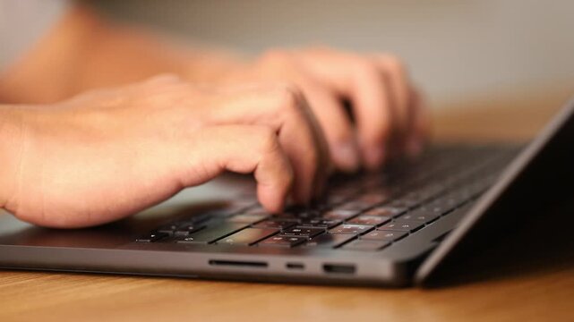 Close up of hands typing on laptop keyboard at wooden desk in soft natural light, modern workspace concept showing productivity, online communication, working remote and digital technology environment