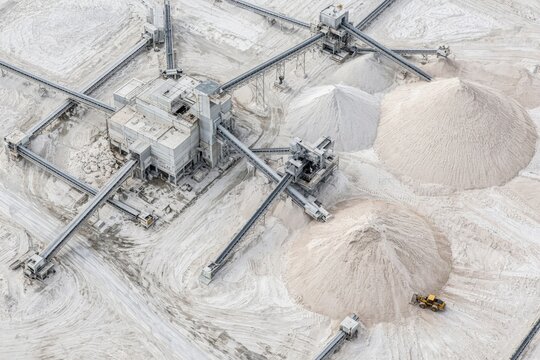 Limestone processing plant with conveyors and white sand cones in bright quarry, aerial view