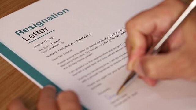 Close up of a person signing a resignation letter document with a pen on a wooden office desk, representing career change, job resignation, and human resources professional agreements