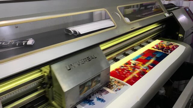 Large format printer head moves across colorful posters at a print shop in Bangladesh