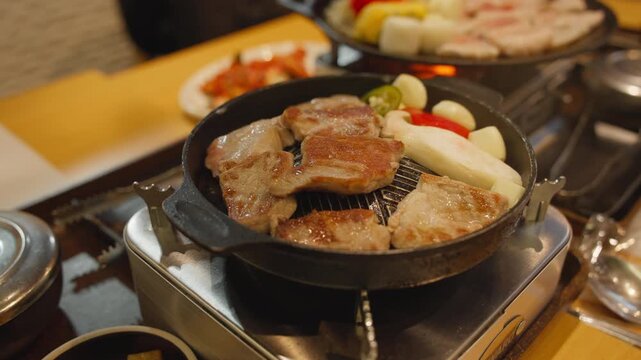 Korean style samgyeopsal grilled pork belly with garlic mushrooms and dipping sauce served on tabletop stove.