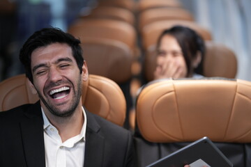 Two passengers looking at one screen share a tablet screen in adjacent seats in adjacent seats on board an airliner, an easy, natural moment in the air, good for connection and travel themes © ultramansk
