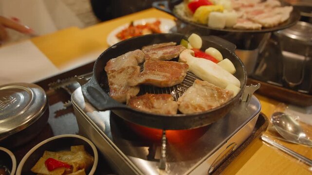 Korean style samgyeopsal grilled pork belly with garlic mushrooms and dipping sauce served on tabletop stove.