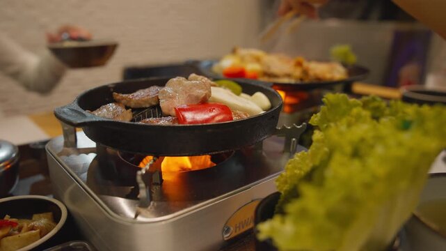 Korean style samgyeopsal grilled pork belly with garlic mushrooms and dipping sauce served on tabletop stove.