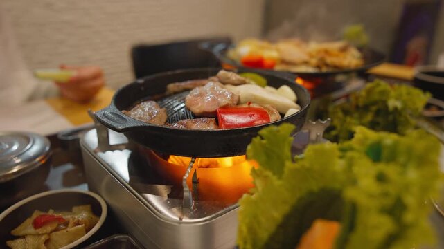 Korean style samgyeopsal grilled pork belly with garlic mushrooms and dipping sauce served on tabletop stove.