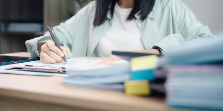 Business professional reviewing performance reports and auditing stack of documents at office desk. Concept of corporate audit, compliance check, data analysis.