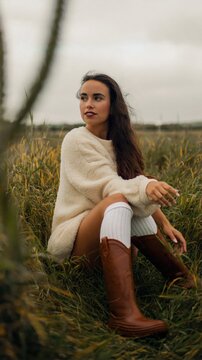 Young woman seated looking sideways in windswept meadow field