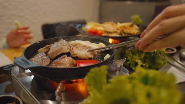 Korean style samgyeopsal grilled pork belly with garlic mushrooms and dipping sauce served on tabletop stove.