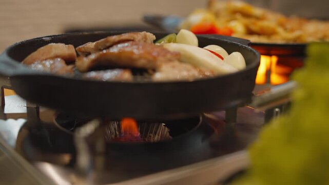 Korean style samgyeopsal grilled pork belly with garlic mushrooms and dipping sauce served on tabletop stove.
