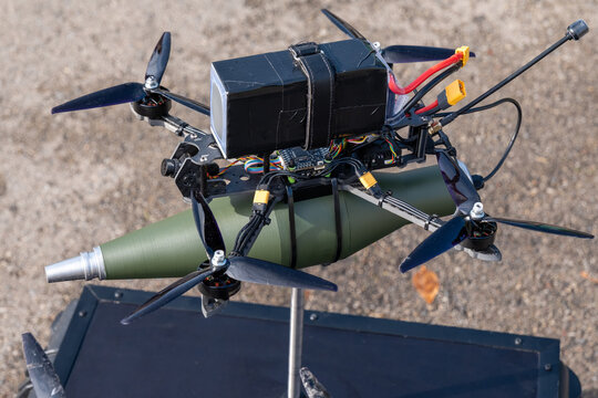 Weaponized quadcopter drone carrying a green bomb-shaped payload outdoors