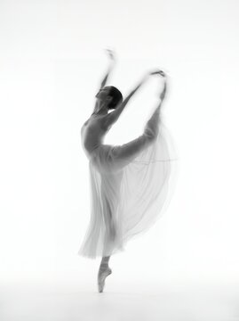 Graceful ballerina in white tutu dress and pointe shoes performing arabesque pose in bright studio. Classical ballet dancer elegant movement, choreography art, and performance concept.