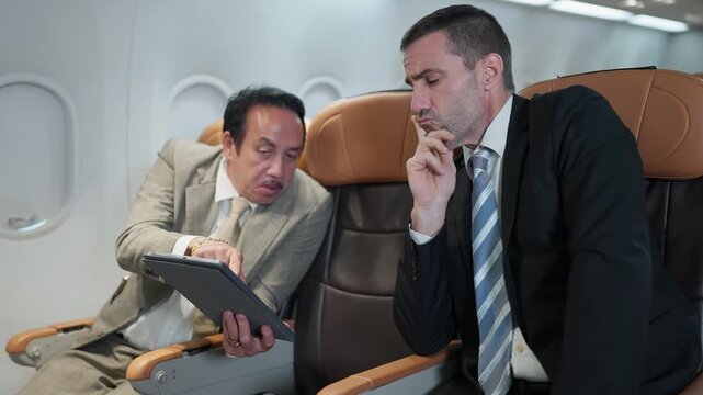 Two businessmen converse mid-flight. One gestures with a tablet, the other listens intently. They appear engaged in professional discussion
