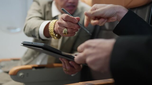 Business meeting concludes with a handshake. One person holds a tablet. The other wears a suit and ring. They appear professional and agreeable