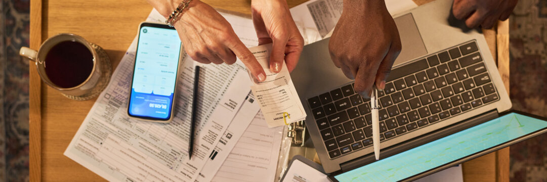 Header of unknown Caucasian woman and African American man managing family budget using laptop and mobile app, top down view. Image suitable for financial planning campaigns