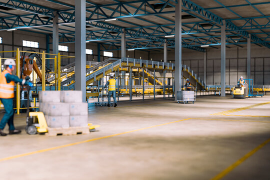 3D Warehouse employee handling packages beside conveyor equipment in large fulfillment center