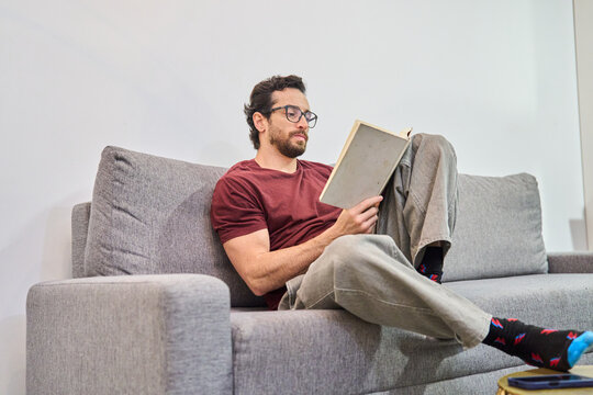 Man relaxing at home reading book on sofa