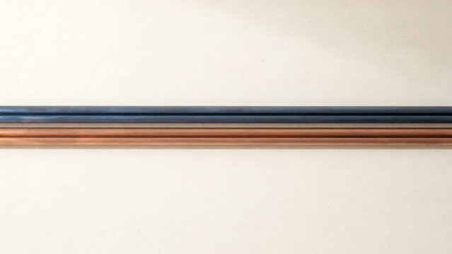 Two Copper and Steel Pipes Lying Parallel Against Neutral Surface with Subtle Lighting