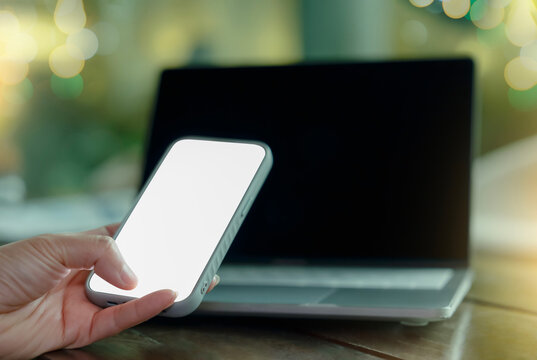 Smartphone mockup, blank screen mobile phone in hand with laptop background, copy space display for app, website, online communication, digital workspace and technology concept.