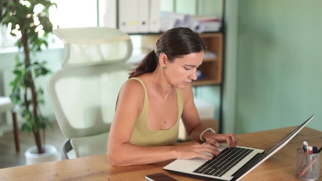 Woman, a qualified specialist, solves work issues with interest while sitting at a table near a laptop. Woman works on a marketing project at work 