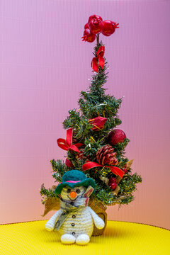 snowman crocheted from yarn, placed on a colorful background next to a Christmas tree
