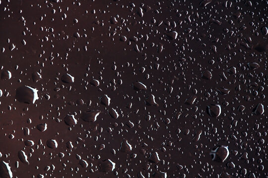 Macro view of clear water droplets scattered over a dark smooth surface with bright highlights.