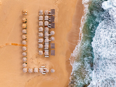 Aerial top view of a beach in Greece with sunbed and sunshade at sunset
