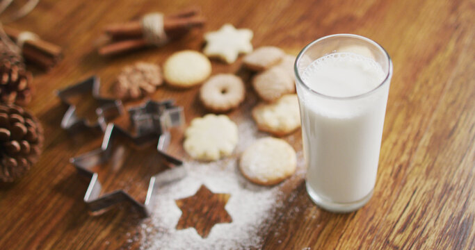 Image of christmas decorations with glass of milk and cookies on wooden background