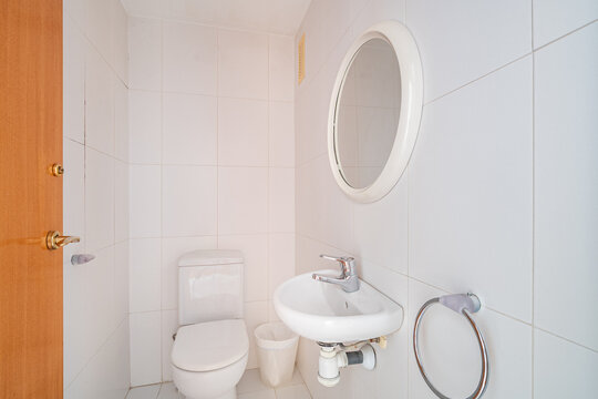 Clean modern white bathroom with toilet, compact wall-mounted sink, round mirror, chrome faucet, and bright tiled walls in minimalist residential interior, with bathroom, toilet, sink, mirror detail