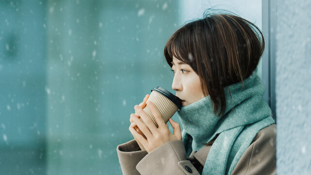 雪が降る街角で飲み物を飲む女性