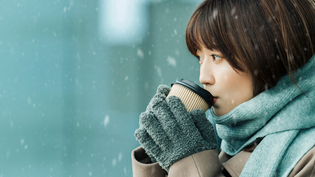 雪が降る街角で飲み物を飲む女性