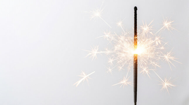 Burning sparkler emits bright light, golden sparks against plain white background. Glowing pyrotechnics create magical atmosphere for festive party celebration. Shiny firework stick burns with