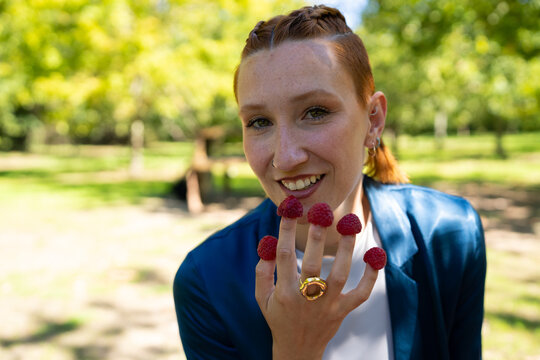 White woman smiling outdoors with raspberries on her fingers in a park