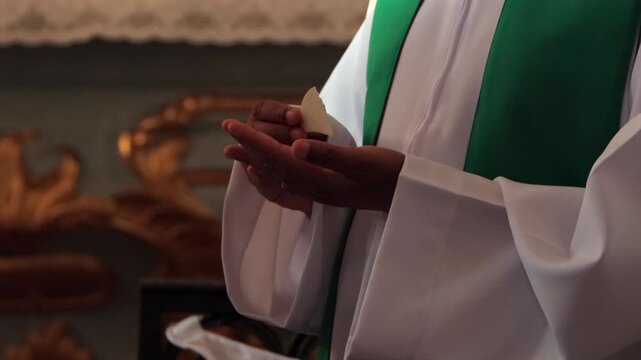 Close up of a Catholic priest in a white alb and green stole holding the consecrated host during Mass, hands only with face not visible