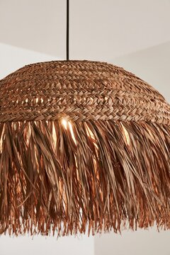 Closeup of woven natural fiber pendant lamp with long loose fringe and warm light in an interior of afro boho kitchen
