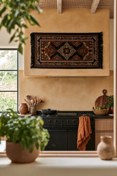 Warm ochre afro boho kitchen with patterned textile, black range, wooden utensils, plants, and window light