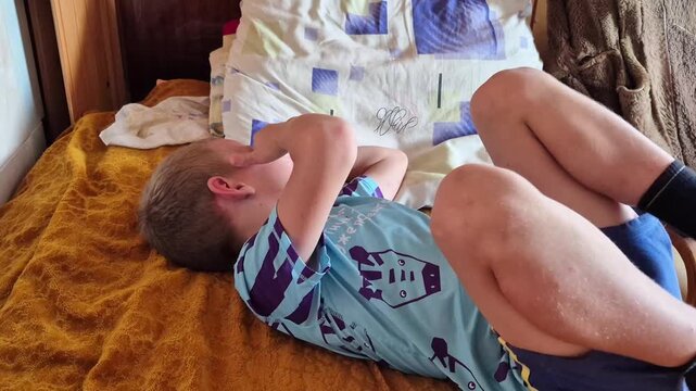 A boy is fooling around on a bed in the bedroom, with his face hidden in his hands.