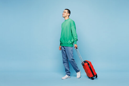 Traveler sideways happy man wear shirt casual clothes hold suitcase bag walk isolated on plain blue background. Tourist travel abroad in free spare time rest getaway Air flight trip journey concept