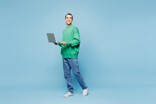 Full body young fun IT middle eastern man he wear green shirt casual clothes hold use work on laptop pc computer isolated on plain pastel light blue cyan background studio portrait. Lifestyle concept.
