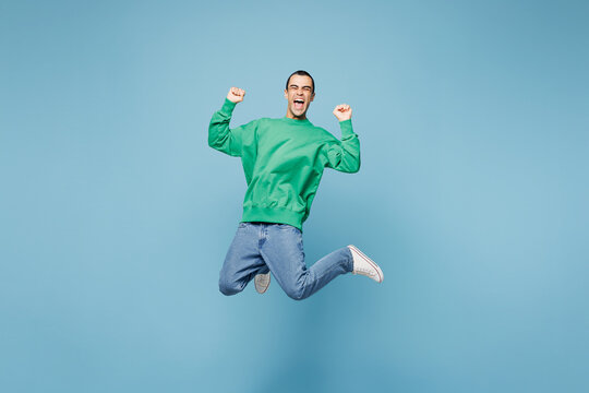 Full body young fun middle eastern man wear green shirt casual clothes jump high do winner gesture clench fist isolated on plain pastel light blue cyan background studio portrait. Lifestyle concept