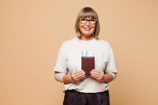 Traveler smiling happy elderly woman wear casual clothes hold passport ticket isolated on plain beige background. Tourist travel abroad in free spare time rest getaway Air flight trip journey concept