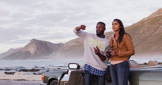 Black couple consults a map by their convertible during a road trip adventure.